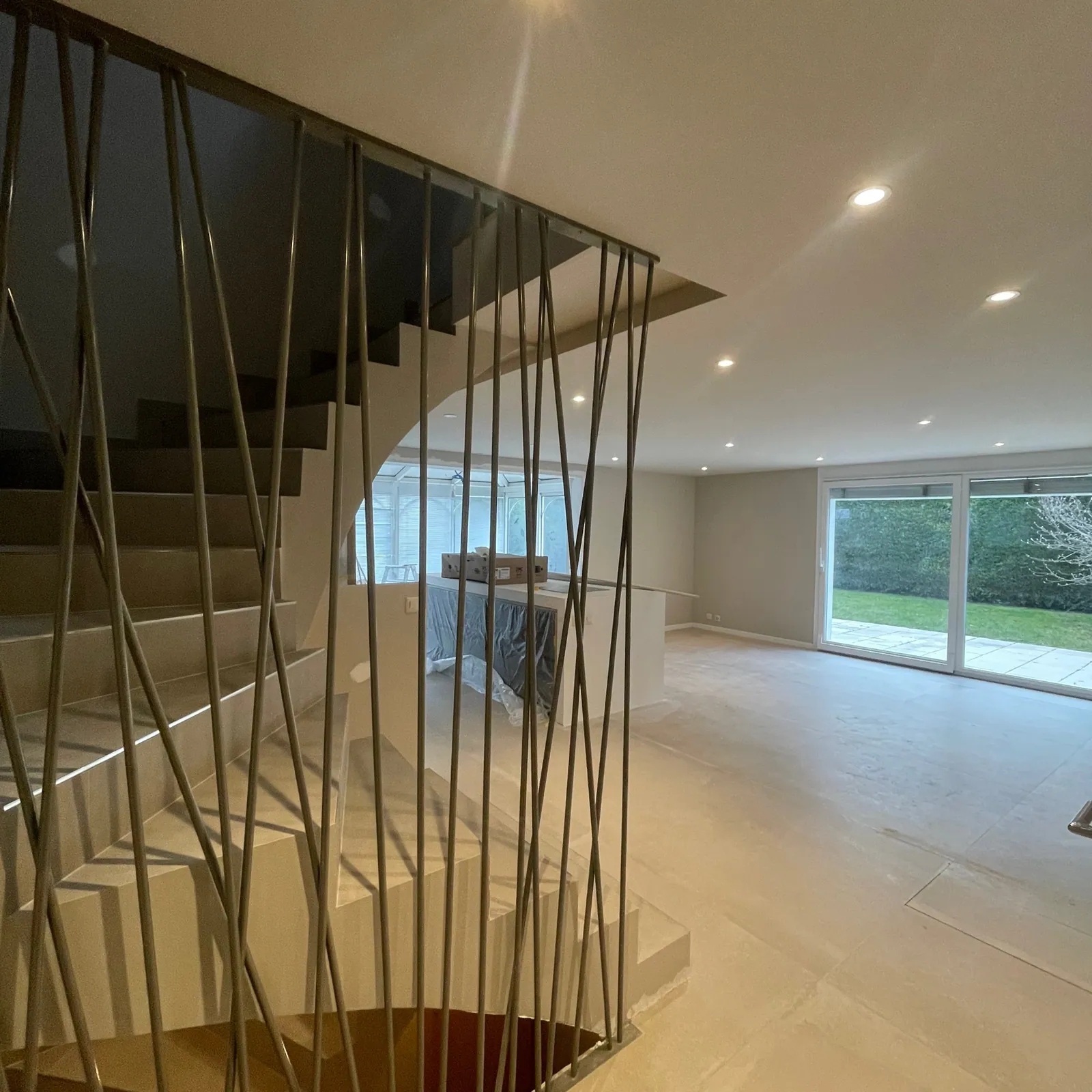 Annecy 104 : escalier à barreaudage métallique et séjour ouvert sur le jardin, pendant les finitions